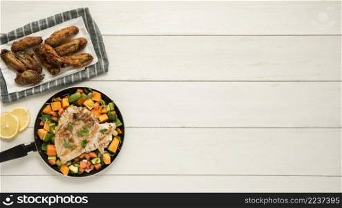 dish with chicken wings frying pan vegetables wooden desk