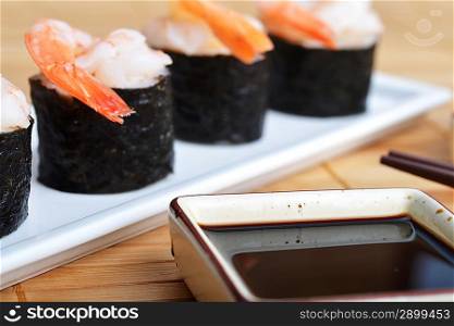 dish with fresh sushi rolls and bowl of sauce on bamboo napkin background
