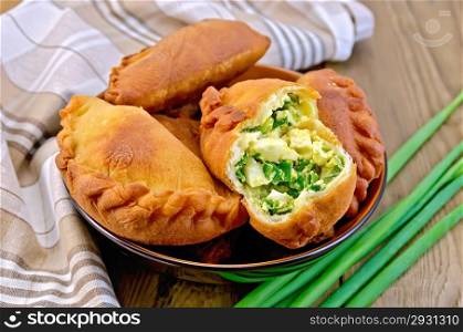 Dish with fried patties with onions and egg, napkin, a bunch of spring onions on a wooden boards background