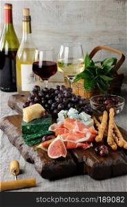Dishes for a snack Antipasto on a wooden board with prosciutto, different kinds of cheese, grapes and figs on a table with wine