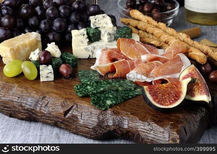 Dishes for Antipasto on a wooden board with prosciutto, different types of cheese, grapes and figs