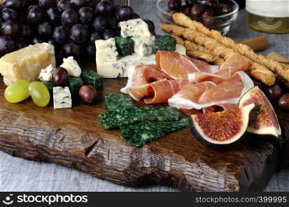 Dishes for Antipasto on a wooden board with prosciutto, different types of cheese, grapes and figs