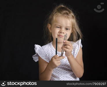 Disheveled girl holding a pair of compasses and a pencil and looks at the compass. Studio, black background.