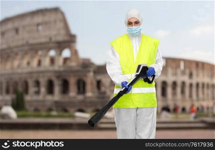 disinfection and pandemic concept - sanitation worker in protective gear or hazmat suit, medical mask, gloves and goggles with pressure washer or sanitizer over coliseum in rome, italy on background. sanitation worker in hazmat with pressure washer
