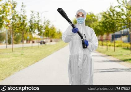 disinfection service and pandemic concept - sanitation worker in protective gear or hazmat suit, medical mask, gloves and goggles with pressure washer or sanitizer over city street background. sanitation worker in hazmat with pressure washer