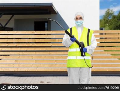 disinfection service and pandemic concept - sanitation worker in protective gear or hazmat suit, medical mask, gloves and goggles with pressure washer or sanitizer over house on city street background. sanitation worker in hazmat with pressure washer
