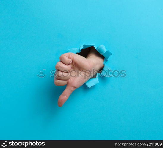 Dislike gesture break through the blue paper. A part of the body sticks out of a hole with ragged edges
