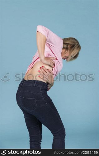 displeased woman suffering from lower back pain blue background