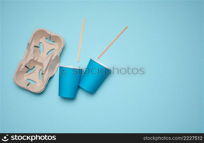 disposable blue paper cups, wood sticks and paper tray on blue background. Takeaway beverage container, top view