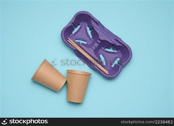 disposable brown paper cups, wood sticks and paper tray on blue background. Takeaway beverage container, top view