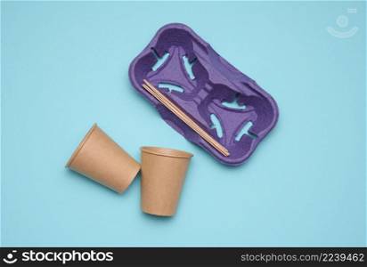 disposable brown paper cups, wood sticks and paper tray on blue background. Takeaway beverage container, top view