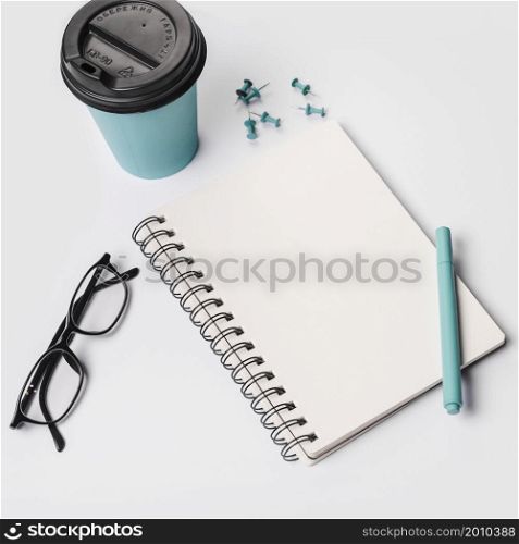 disposable coffee cup pen eyeglasses spiral notepad thumbtack pins white background