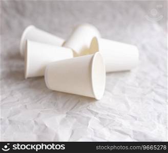 disposable cups made of white paper are laid out on gray crumpled paper in a geometric pattern