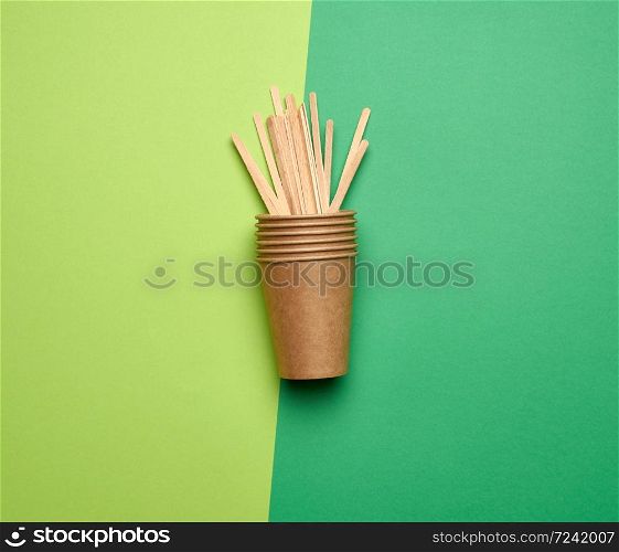 disposable empty cups of brown craft paper and wooden sticks for stirring the drink on a green background, top view, plastic rejection concept, zero waste