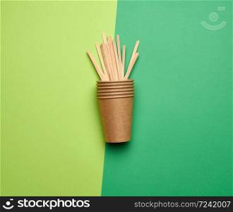 disposable empty cups of brown craft paper and wooden sticks for stirring the drink on a green background, top view, plastic rejection concept, zero waste