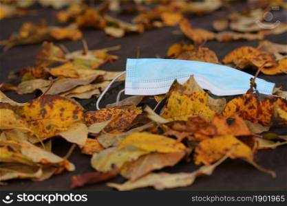 Disposable face mask lying on the street around leaves in autumn during Covid19 pandemic .. Disposable face mask lying on the street around leaves in autumn during Covid19 pandemic