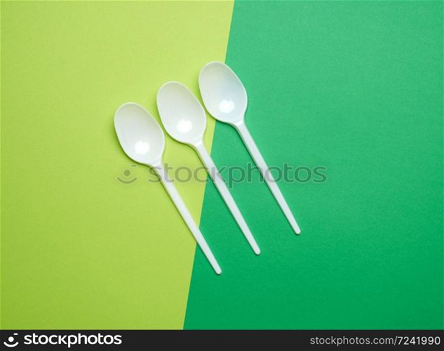 disposable plastic white spoons on a green background, top view