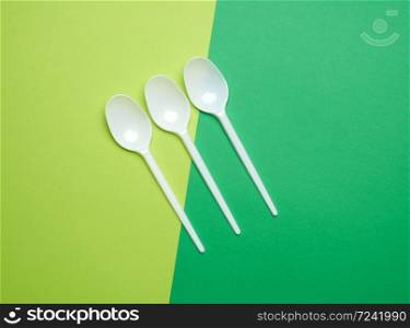 disposable plastic white spoons on a green background, top view