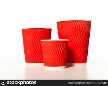 Disposable red paper coffee cups of different sizes standing in a row on a white background, mockup for design for espresso, cappuccino, latte. Set of paper cups