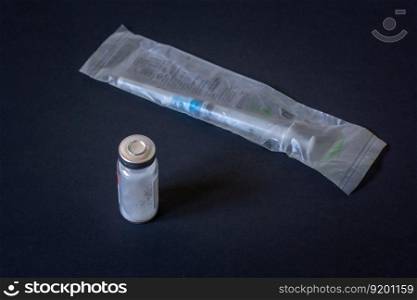 Disposable syringe in package and vial with white powder. Dark background. Horizontal.