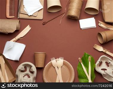 disposable tableware from brown craft paper, green leaf on a brown background. View from above, plastic rejection concept, zero waste, copy space