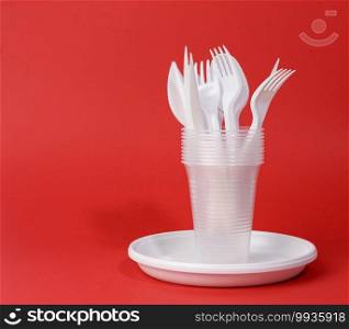 disposable white plastic tableware plates, cups, forks and knives on a red background, picnic set