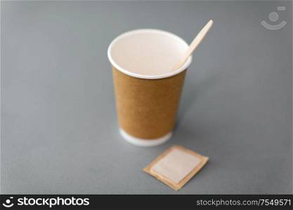 dispose, recycling and ecology concept - takeaway paper coffee cup with spoon and sugar bag on grey background. disposable paper coffee cup with spoon and sugar
