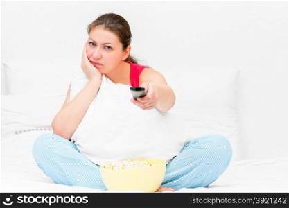 dissatisfied girl in pajamas with a TV remote control