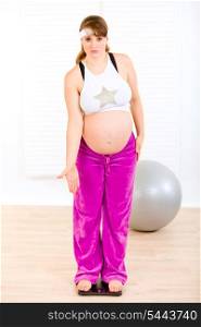 Dissatisfied with her weight pregnant female standing on weight scale at home&#xA;