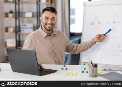 distance education, school and remote job concept - happy smiling male chemistry teacher with laptop computer having online class and showing molecular model on flip chart at home office. chemistry teacher with laptop having online class