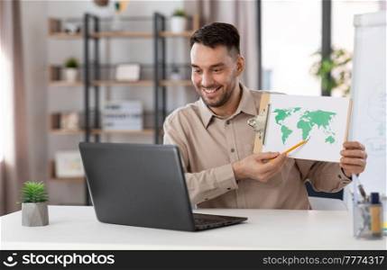 distance education, school and remote job concept - happy smiling male geography teacher with world map and laptop computer having online geography class at home office. teacher with world map having online class at home