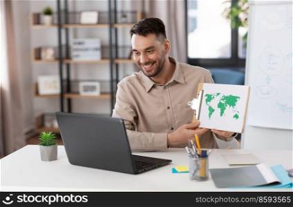 distance education, school and remote job concept - happy smiling male geography teacher with world map and laptop computer having online geography class at home office. teacher with world map having online class at home
