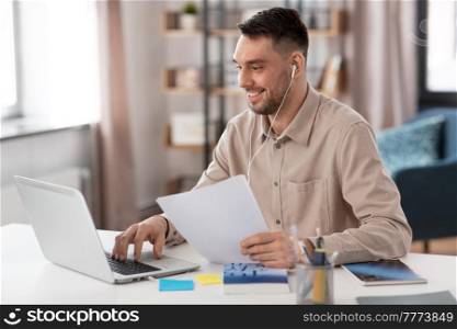 distance education, school and remote job concept - happy smiling male teacher or student with laptop computer and earphones working or learning at home office. teacher with laptop and earphones working at home