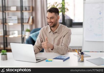 distance education, school and remote job concept - happy smiling male teacher with laptop computer having online class at home office showing thumbs up. teacher with laptop having online class at home