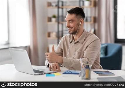 distance education, school and remote job concept - happy smiling male teacher or student with laptop computer and earphones having online class or video call at home office. teacher with laptop having online class at home