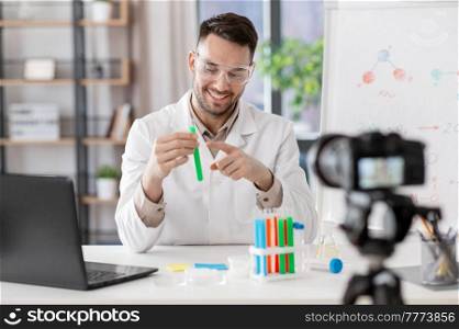 distance education, school and video blogging concept - happy smiling male chemistry teacher with camera and test tube having online class at home office. chemistry teacher with camera having online class