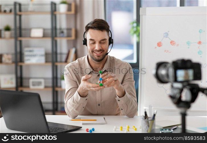 distance education, school and video blogging concept - happy smiling male chemistry teacher in headset with camera and molecule model having online class at home office. chemistry teacher with camera having online class