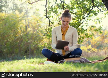 Distance education. Sitting woman using ipad during autumn fun outdoors