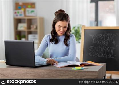 distant education, online school and people concept - happy smiling female teacher with laptop computer and notebook working from home. teacher with laptop and notebook working from home