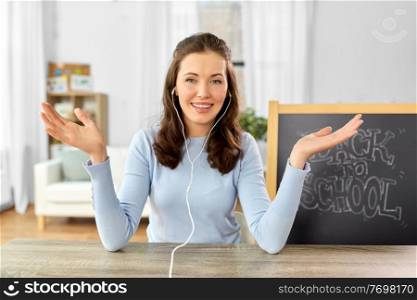 distant education, primary school and teaching concept - female teacher in earphones having online class or video call at home. teacher having online class or video call at home
