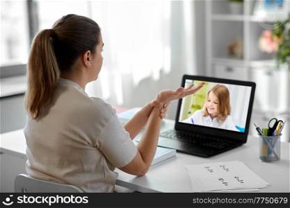 distant education, remote job and health concept - tired female teacher having video call or online class with student girl on laptop computer screen and touching her wrist at home office. tired teacher with laptop touching wrist at home