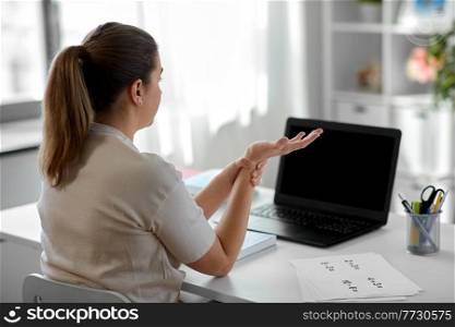 distant education, remote job and health concept - tired female teacher with laptop computer touching her wrist at home office. tired teacher with laptop touching wrist at home