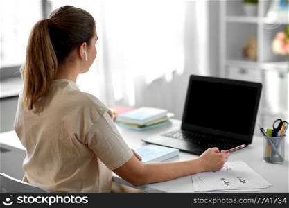 distant education, remote job and people concept - female math teacher with laptop computer and earphones working at home office. math teacher with laptop and earphones at home