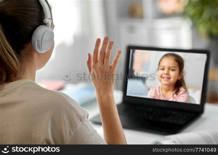 distant education, remote job and people concept - female teacher in headphones with laptop computer having video call or online class with little student girl at home and waving hand. teacher with laptop having video call with girl