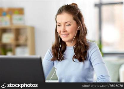 distant education, remote job and people concept - happy smiling female teacher with laptop computer and earphones having online class or video call at home office. teacher with laptop having online class at home