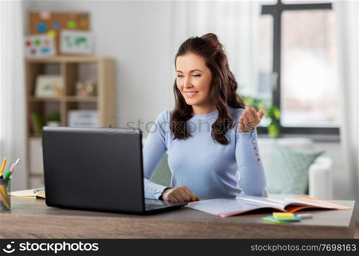 distant education, remote job and people concept - happy smiling female teacher with laptop computer having online class or video call at home office. teacher with laptop having online class at home