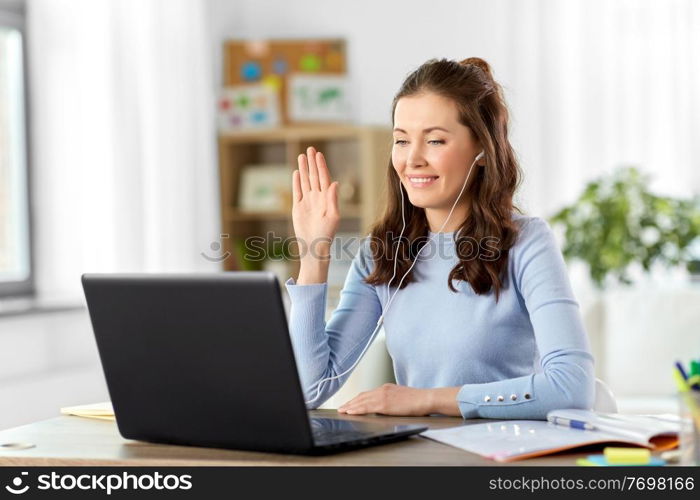 distant education, remote job and people concept - happy smiling female teacher with laptop computer and earphones having online class or video call at home office. teacher with laptop having online class at home