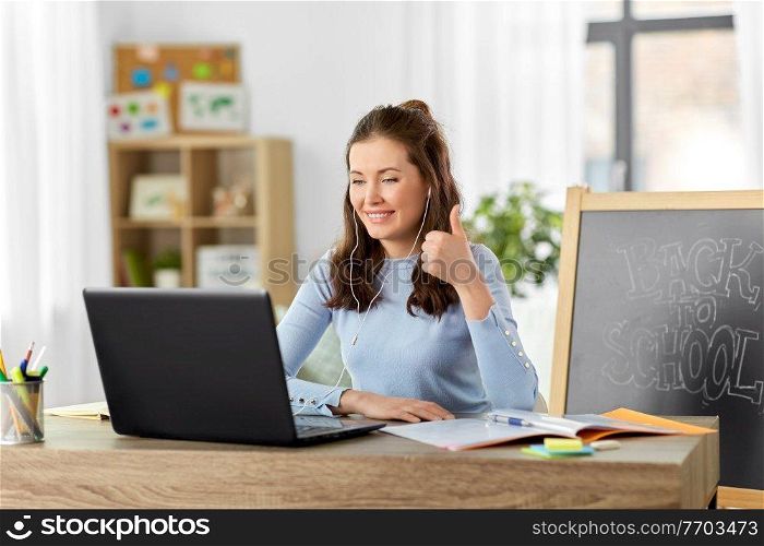 distant education, remote job and people concept - happy smiling female teacher with laptop computer and earphones having online class or video call and showing on gesture at home office. teacher with laptop having online class at home
