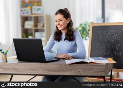 distant education, remote job and people concept - happy smiling female teacher with laptop computer and wireless earphones having online class or video call at home office. teacher with laptop having online class at home