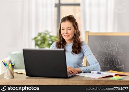 distant education, remote job and people concept - happy smiling female teacher with laptop computer and earphones having online class or video call at home office. teacher with laptop having online class at home